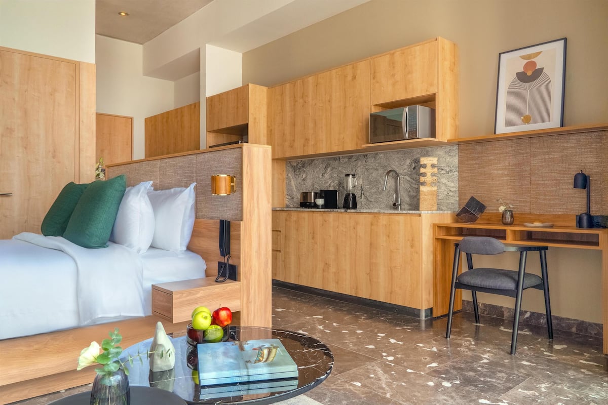 Moderni hotellihuone, jossa on sänky, työpöytä, keittotila ja ruokapöytä.