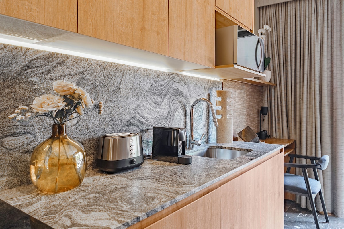 A kitchen with a marble countertop, a toaster, a kettle, a sink, and a vase with flowers.