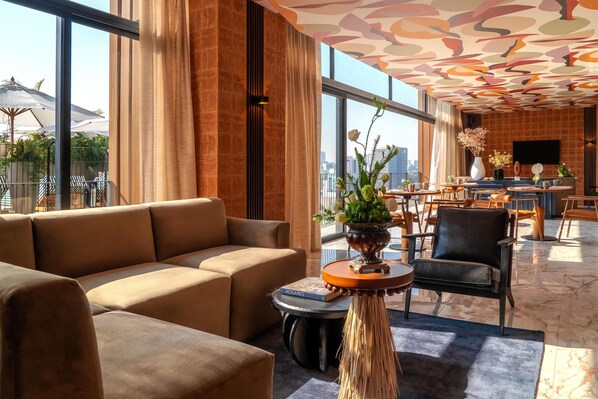 A modern hotel lobby with a large sofa, a round table with a vase, and a city view through large windows. - NH Guadalajara Studios (Guadalajara)