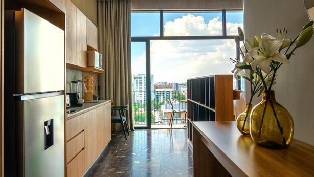 A modern kitchen with a large window, a refrigerator, and a vase with flowers on the counter. - NH Guadalajara Studios (Guadalajara)