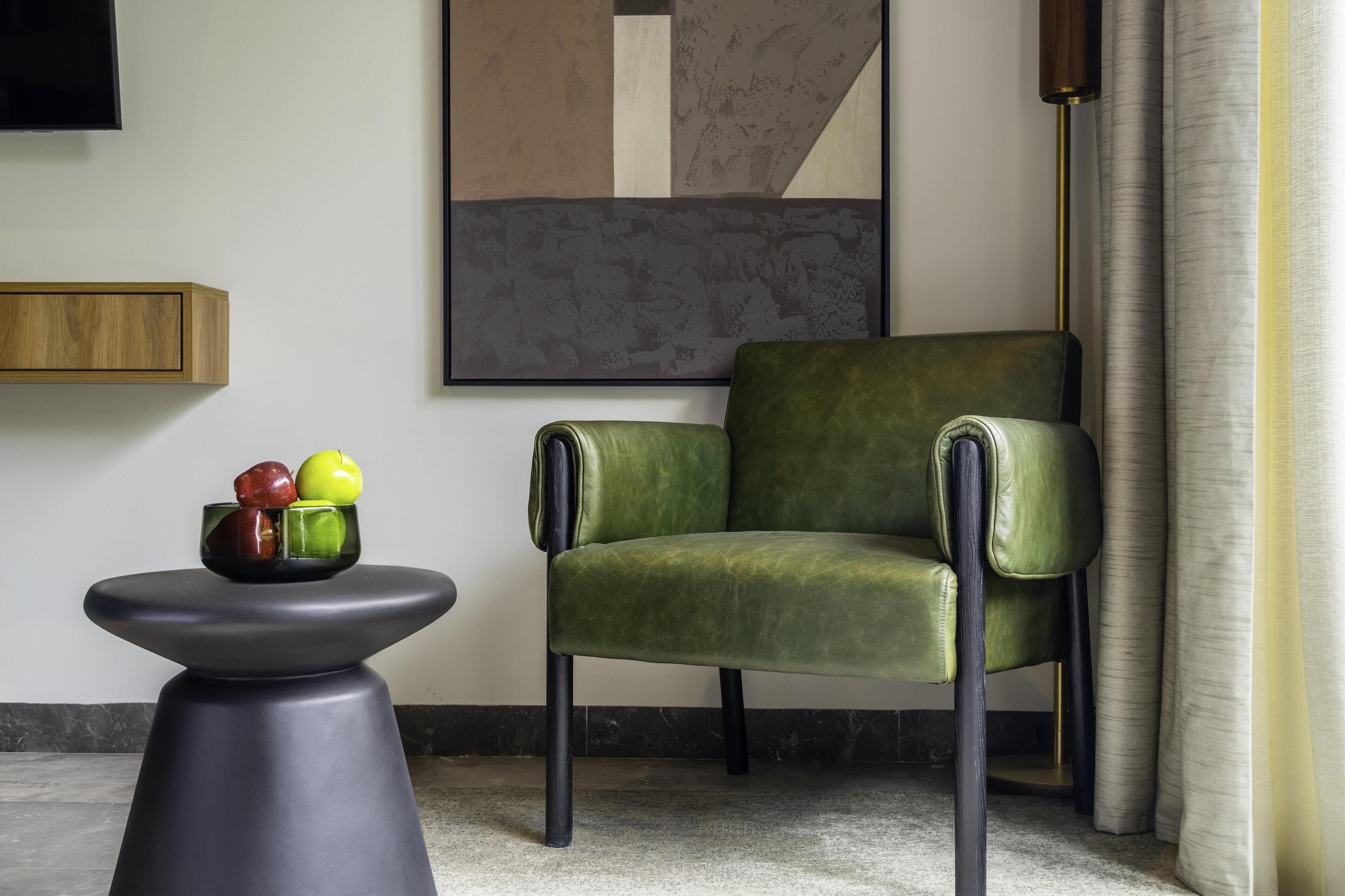 Un sillón verde, una mesa negra con un frutero y un cuadro abstracto grande en la pared.