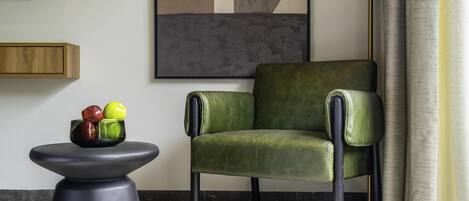 Un sillón verde, una mesa negra con un frutero y un cuadro abstracto grande en la pared.