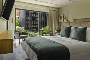 A hotel room with a large bed, a desk, a chair, a TV, and a balcony with a view of greenery. - NH Guadalajara Studios (Guadalajara)