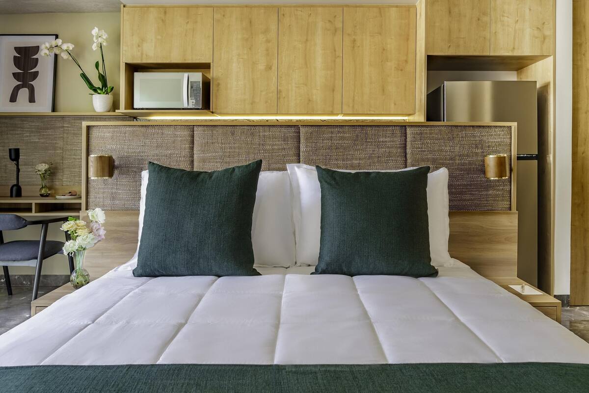 Moderni hotellihuone, jossa on suuri sänky, puinen pääty, pieni työpöytä ja mikroaaltouuni.