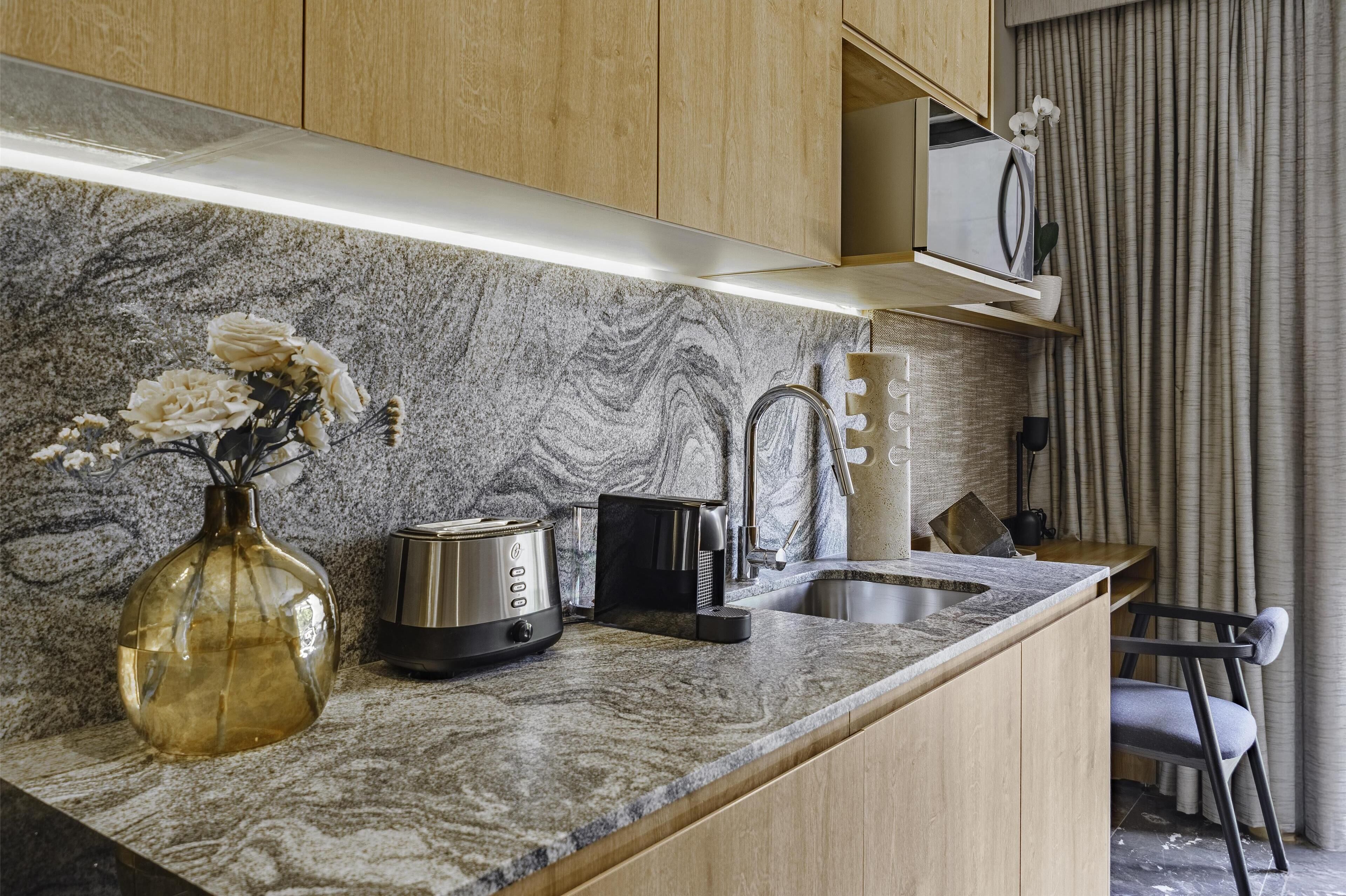 A modern kitchen with a marble countertop, a toaster, a kettle, and a vase with flowers.