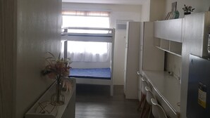 A compact kitchenette with a built-in fridge, a small dining table with chairs, and a single bed with a window above it. - Studio Unit Around Recto U-belt (Manila)