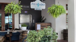 A restaurant named Pescado Seafood Grill with hanging plants, a wooden counter, and a sign indicating it was established in 2018.