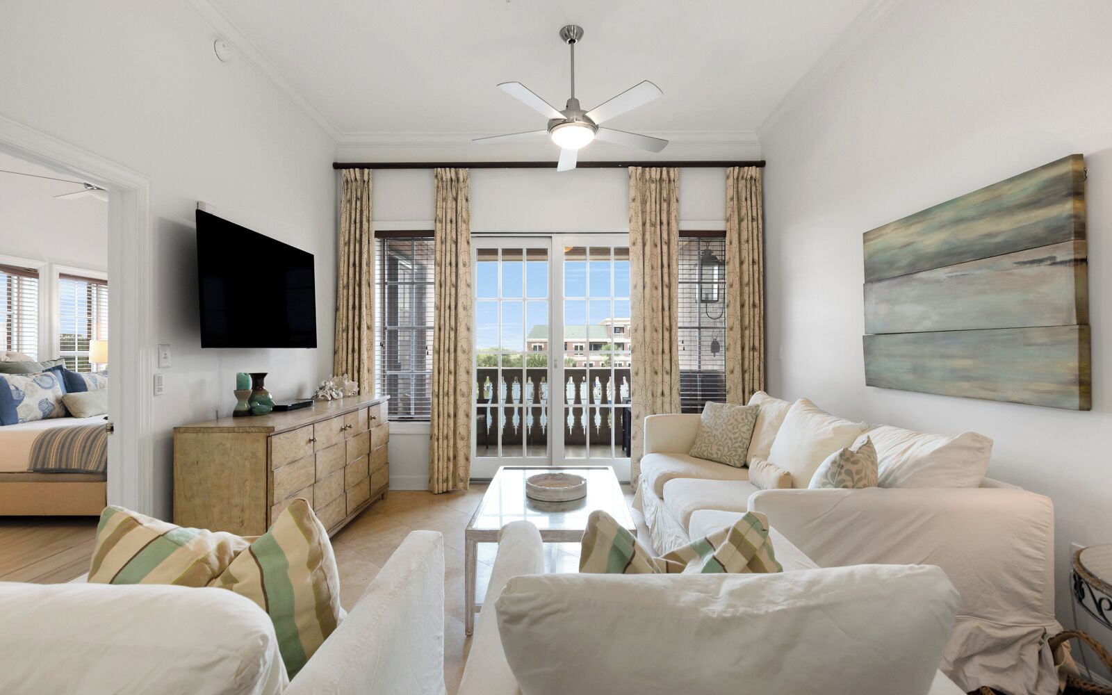 A living room with a TV, sofa, and a balcony with curtains.
