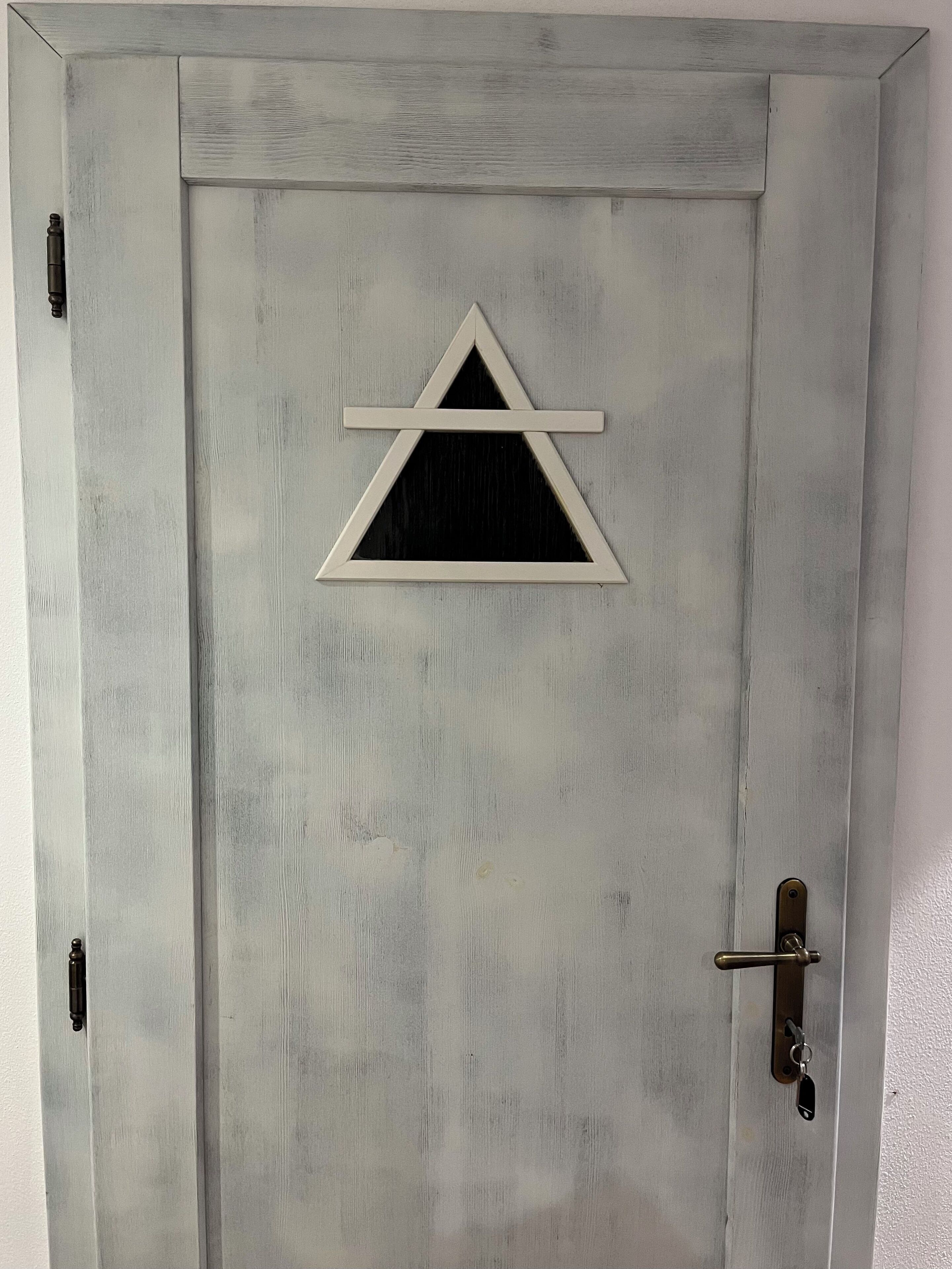 Una puerta con un ventanal triangular y una cerradura con ojo de cerradura.