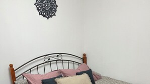 Een net opgemaakt bed met een geborduurd sprei, meerdere kussens en een decoratief wandobject.
