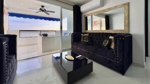 Una sala de estar moderna con un sofá azul oscuro, una mesa de centro de vidrio y un espejo grande en la pared.