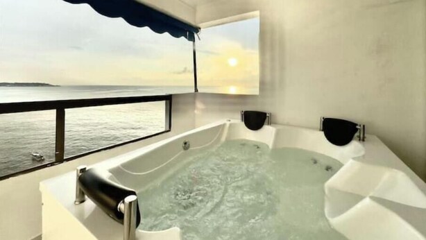 Un baño moderno con una bañera grande, una ventana con vista al mar y un ventilador de techo.