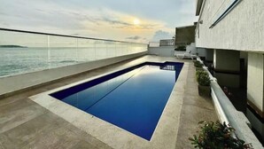 Una piscina en la azotea con vistas despejadas al mar y una puesta de sol al fondo.
