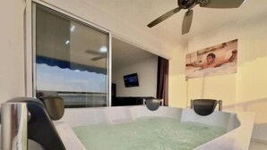 Un baño moderno con una bañera grande, un ventilador de techo y un televisor al fondo.