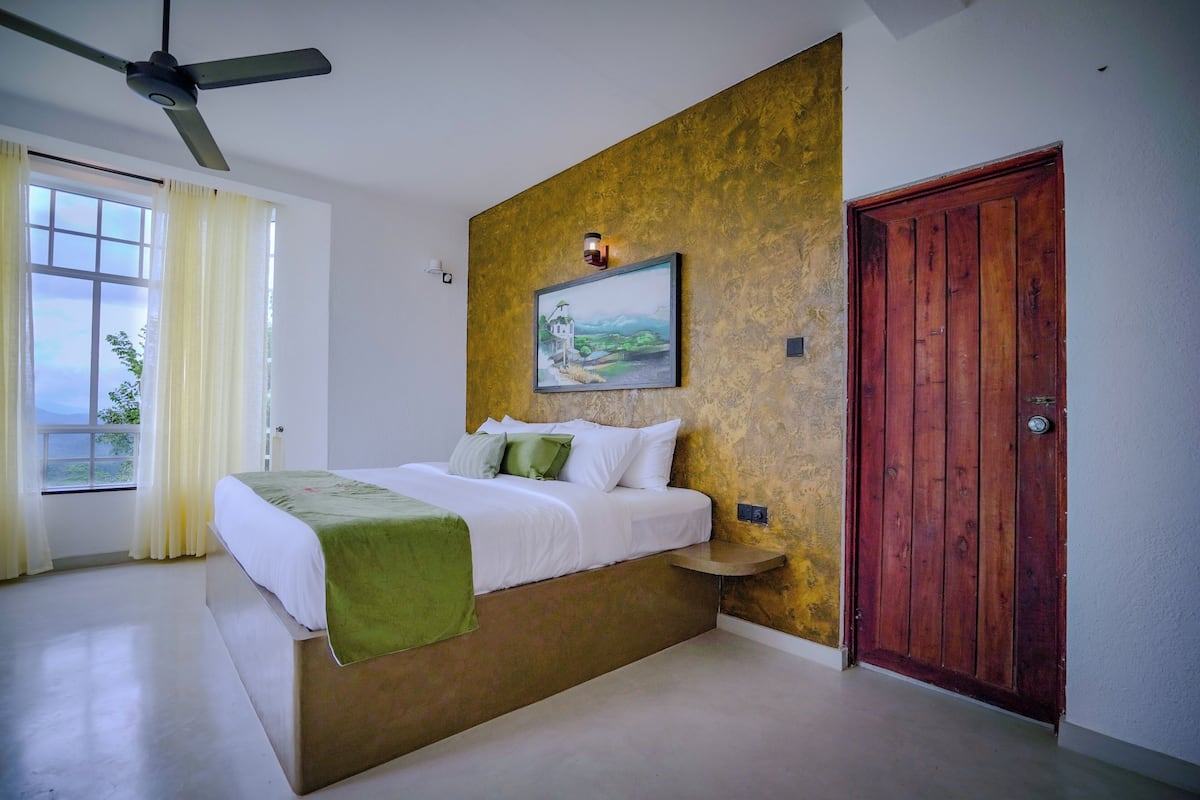 A bedroom with a bed, a wooden door, a painting on the wall, and a window with curtains.