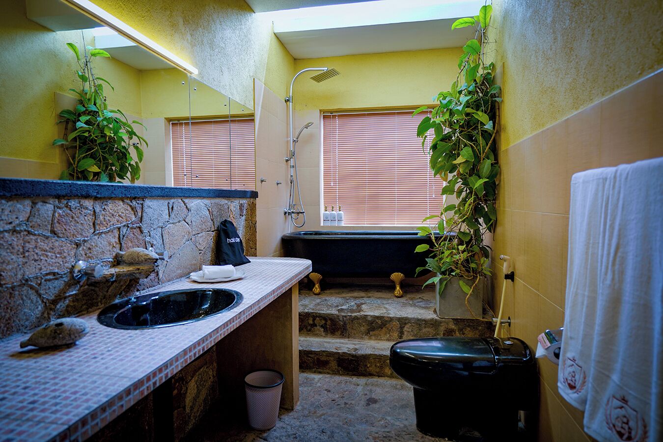 A bathroom with a stone sink, a black bathtub, and a shower.