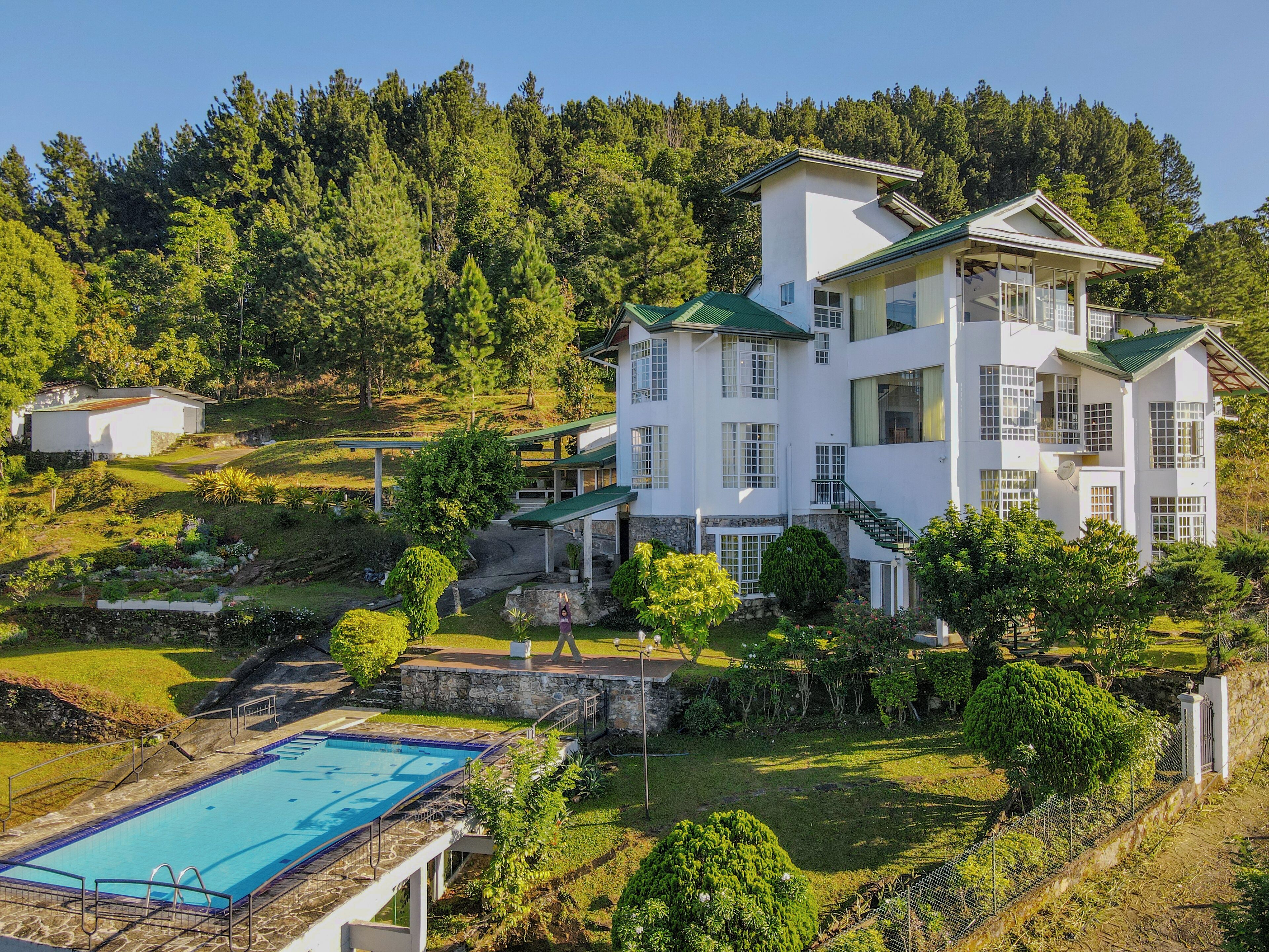 Un grand bâtiment blanc doté d’une piscine, entouré d’une végétation luxuriante et de collines.