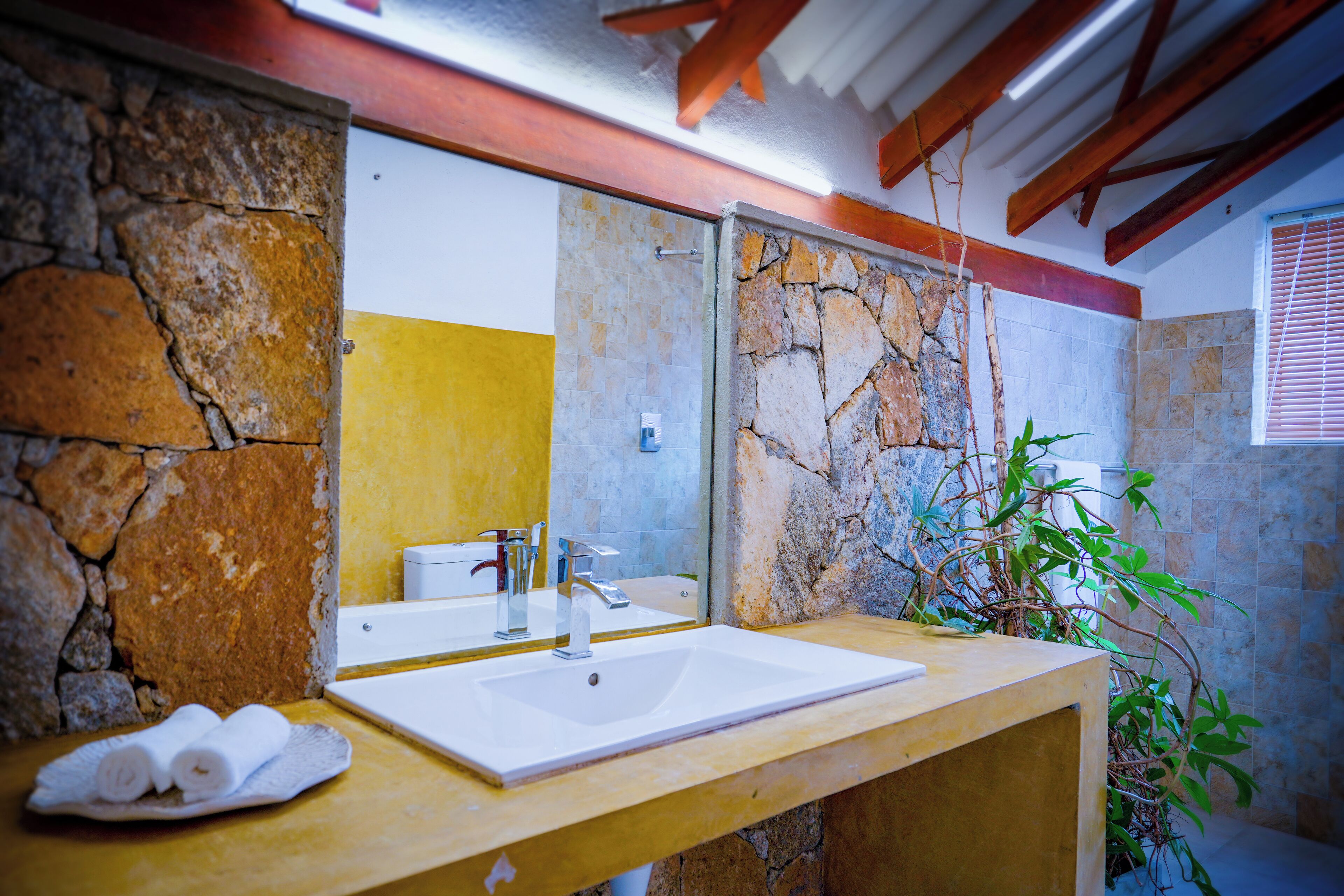 Un baño con pared de piedra, un lavabo blanco y un espejo.