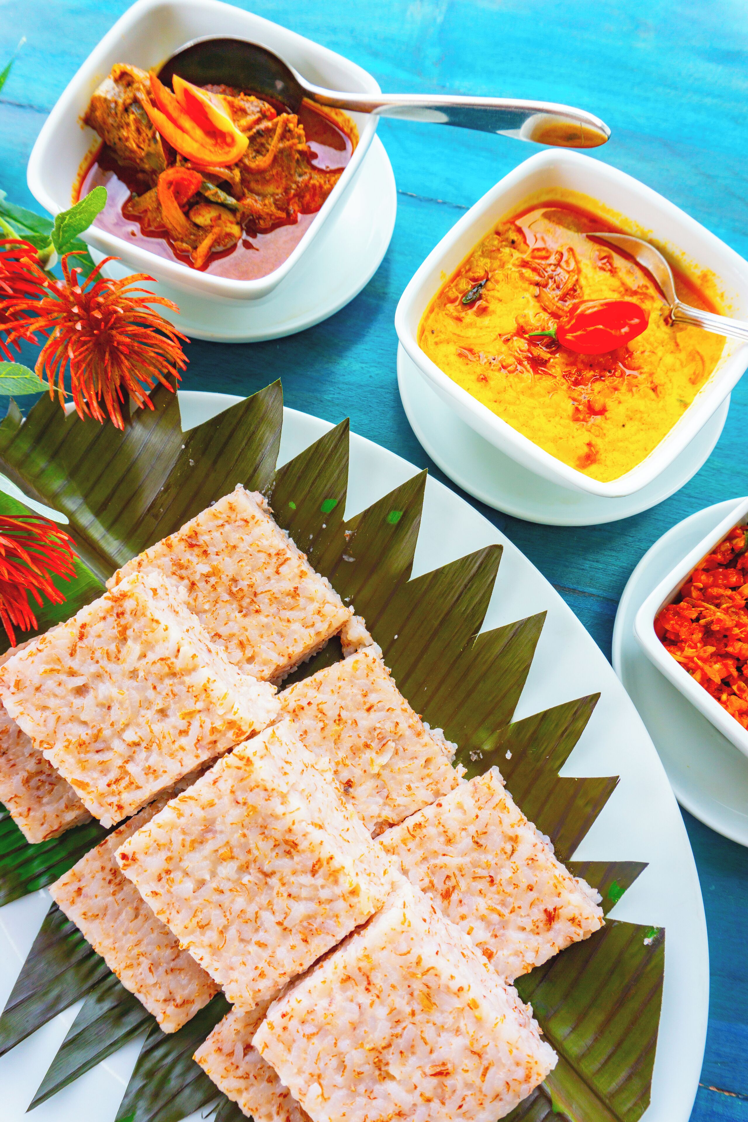A plate of food with a banana leaf, a bowl of soup, and a bowl of curry.
