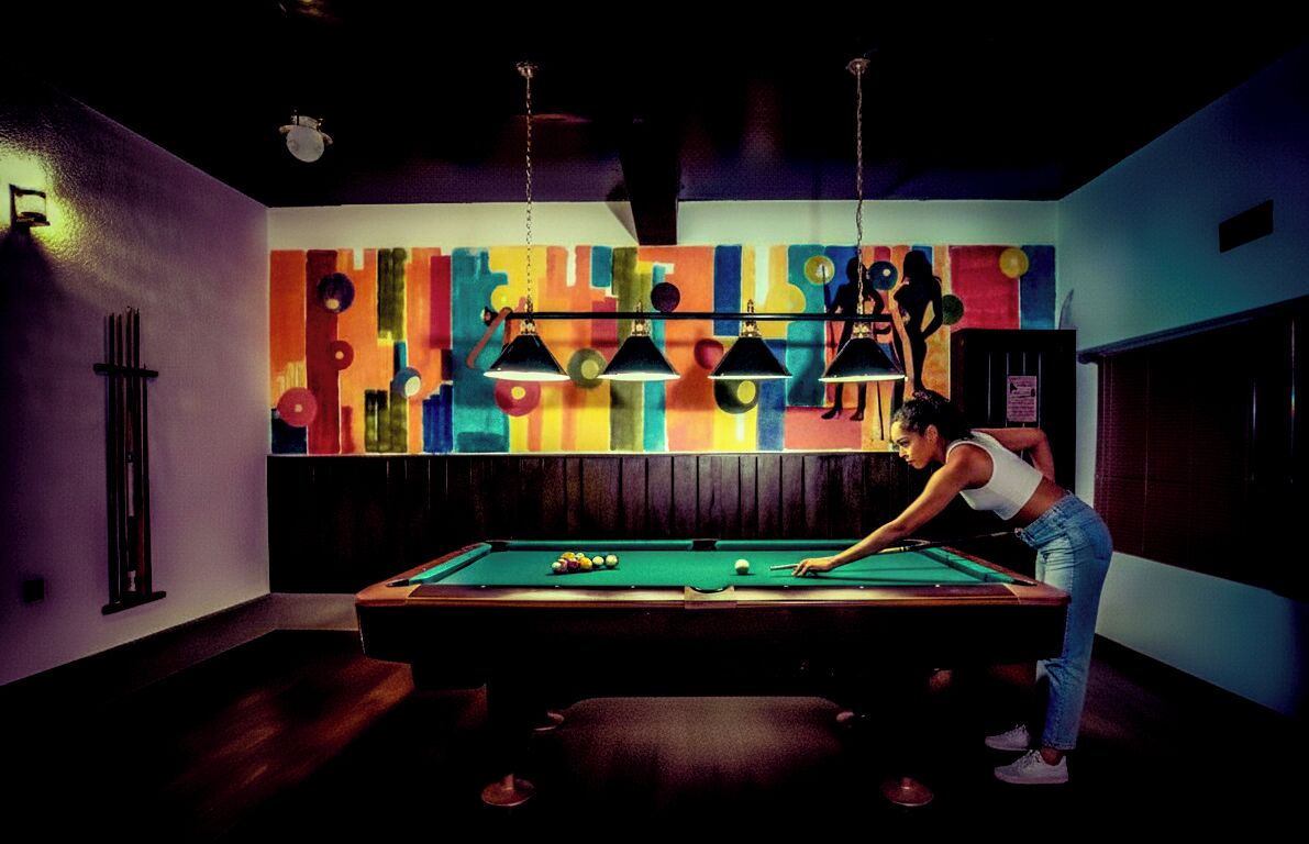 A pool table in a room with a colorful abstract mural on the wall and pendant lighting.