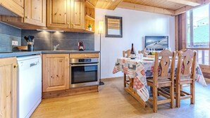 Une cuisine dotée de meubles en bois, d’un lave-vaisselle, d’un four et d’un coin repas avec une table dressée pour deux personnes.