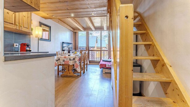 Un intérieur en bois comprenant une cuisine, un coin repas et un escalier menant à une chambre située en mezzanine.