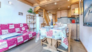 Un intérieur chaleureux et rustique, avec un plafond en bois, une table à manger dressée pour deux personnes et un canapé recouvert d’un tissu à motifs.