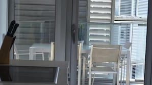 A view of a balcony with white chairs and a table, a glass door, and a window with blinds.
