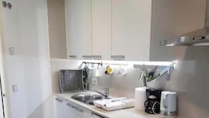 A compact kitchen with a dishwasher, a sink, a stove, and a coffee maker.