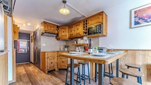 Een compacte keuken met houten kastjes, een magnetron en een eethoek met krukken.