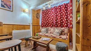 Een knus ingerichte kamer met een houten bankje, een bank met decoratieve kussens en een rood gordijn met hartmotieven.
