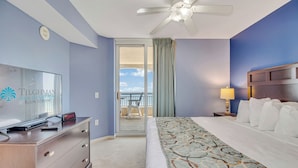 A hotel room with a bed, a dresser, a television, and a view of the balcony. - 3BR- 14th floor- Oceanview Corner Condo (North Myrtle Beach)