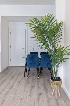 Ein Essbereich mit einer weißen Tür, einem Tisch mit blau gepolsterten Stühlen und einer Topfpflanze auf einem Holzständer.