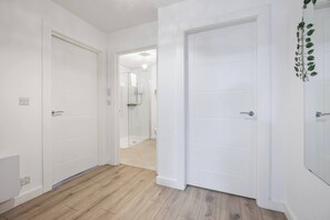 Ein Flur mit weißen Türen, einer Duschkabine und einer Pflanze an der Wand.