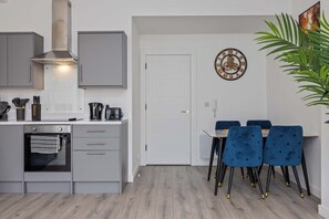 Eine moderne Küche mit grauen Schränken, einem eingebauten Backofen und einem Essbereich mit blauen Stühlen und einem weißen Tisch.