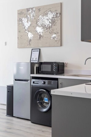 Une cuisine compacte équipée d’un lave-linge, d’un four à micro-ondes et d’un réfrigérateur.