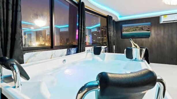 A modern bathroom with a large bathtub, a vanity with a mirror, and a window with a city view.
