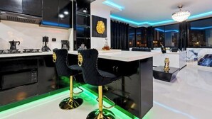 A modern kitchen with black cabinets, a white countertop, and two black bar stools with gold accents.