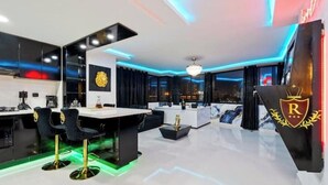 A modern kitchen with black cabinets, a white countertop, and a bar area with two black bar stools.