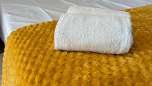 Un lit bien fait, avec du linge de lit blanc, un coussin à motifs jaunes et une serviette blanche pliée, posée sur une couverture jaune à texture particulière.