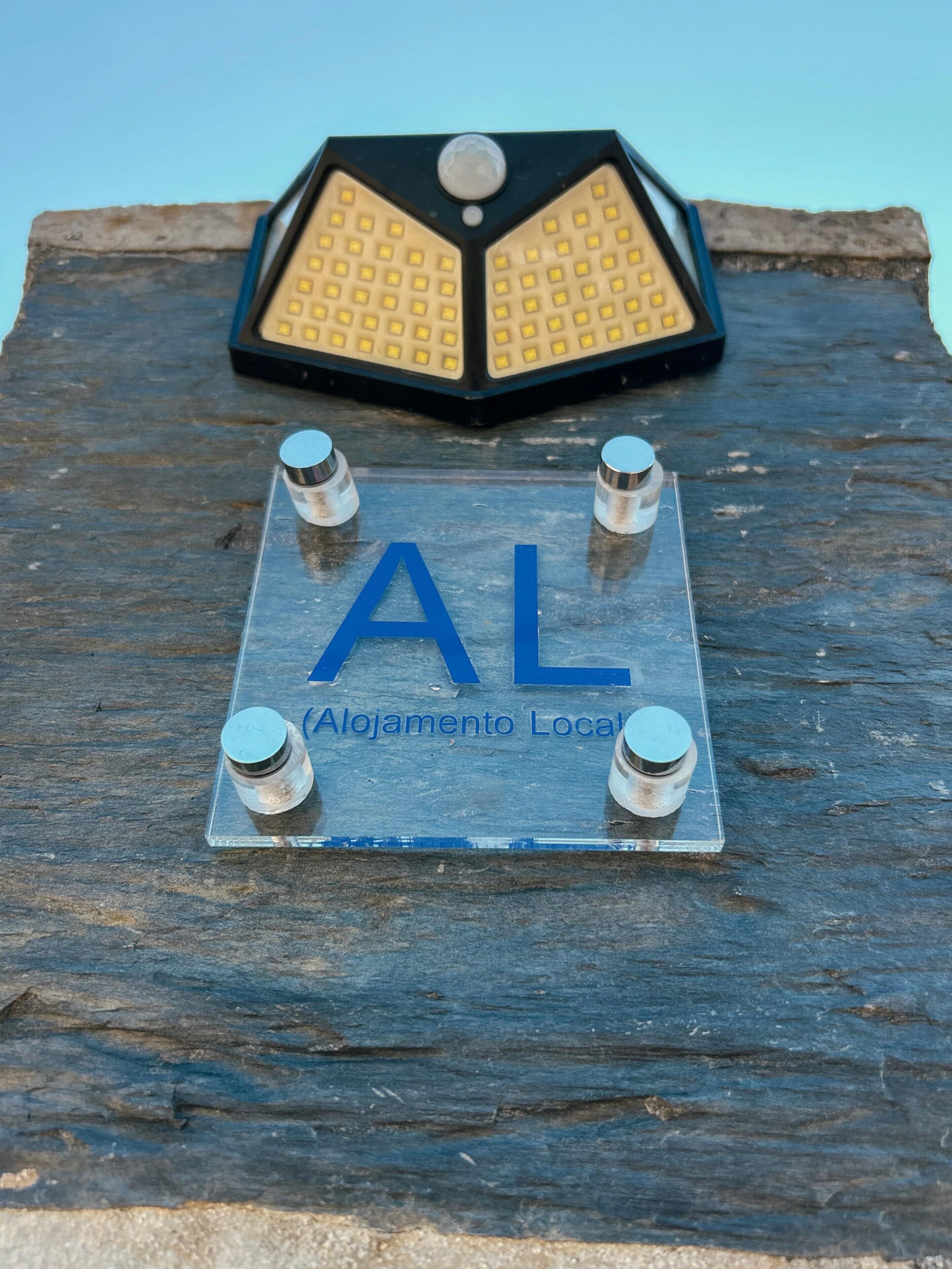 A metal plaque with 'AL' and 'Alojamento Local' on a wooden surface.