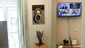 A modern dining area with a wooden table and white chairs, a TV mounted on the wall, and a decorative wall piece.