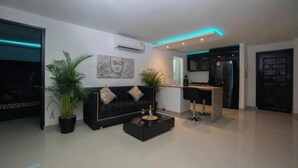 A modern living room with a black sofa, a coffee table, and a potted plant. There is a kitchen area visible in the background. - Tropical One-Bed Oasis (CARTAGENA BOLIVAR)