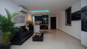 A modern living room with a black sofa, a coffee table, and potted plants. There is a kitchen area in the background with a black countertop and cabinets. - Tropical One-Bed Oasis (CARTAGENA BOLIVAR)