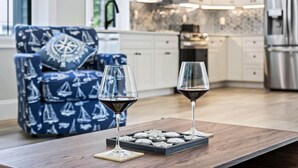 Eine moderne Küche mit weißen Schränken, einer Mikrowelle und einem Edelstahl-Kühlschrank. Auf einem Holztisch stehen zwei Weingläser und eine Keksplatte.