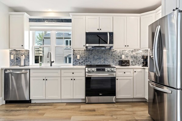 A modern kitchen with white cabinetry, stainless steel appliances, and a large window providing natural light.