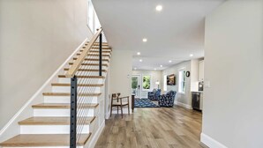 Eine Treppe mit Holzboden und Metallgeländer, die zu einem Wohnbereich mit gepunkteter Couch und Esstisch führt.