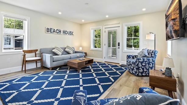 Ein Wohnzimmer mit einem blauen Teppich mit Muster, einem grauen Sofa, einem blauen Ohrensessel mit Muster und einem Holztisch.