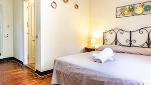 A hotel room with a bed, a nightstand with a lamp, a door, and a wall decoration. - Room 'Oliva' with Shared Garden and Wi-Fi (Gavorrano)