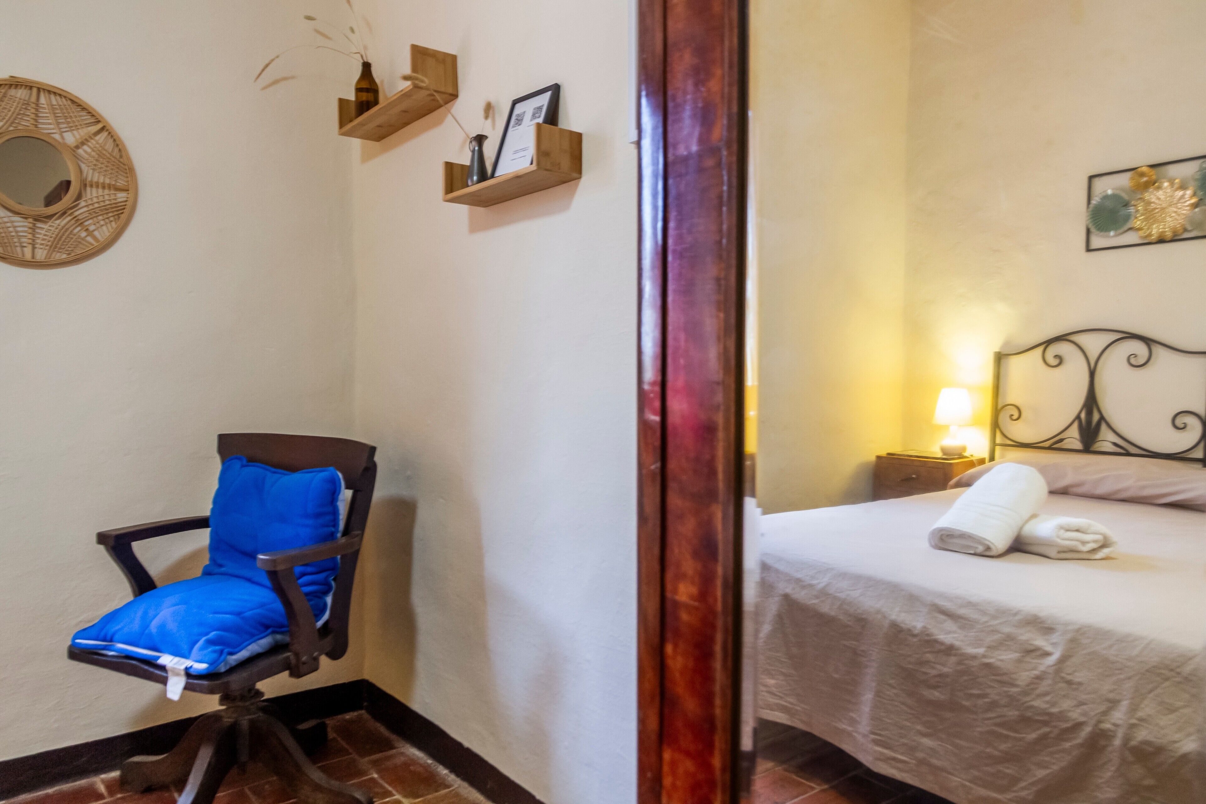 A room with a bed, a chair, a bedside table with a lamp, and wall decorations.